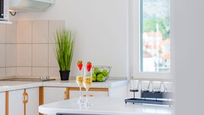 Une cuisine moderne avec un plan de travail blanc, une plante en pot, un saladier de fruits et deux verres de champagne garnis de fraises.