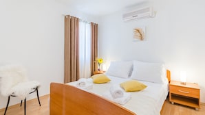 Une chambre d’hôtel avec un lit en bois, du linge de lit blanc, une table de chevet avec une lampe, une chaise et une fenêtre avec des rideaux.