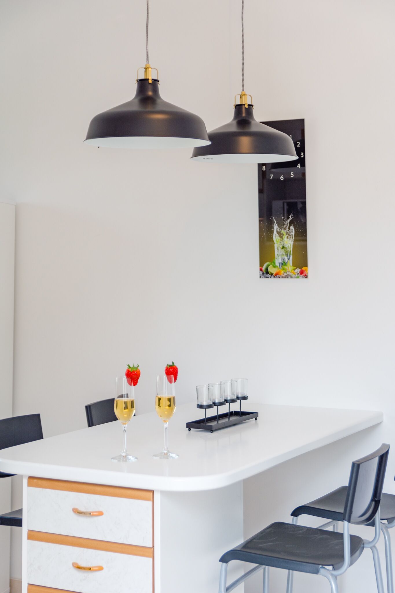 Eine moderne Küche mit einer weißen Kücheninsel, zwei Pendelleuchten und einem gerahmten Bild an der Wand.