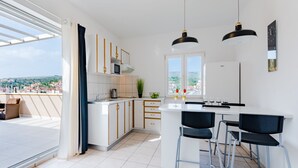 Une cuisine moderne dotée d’un grand îlot central, de meubles blancs et offrant une vue sur la ville.