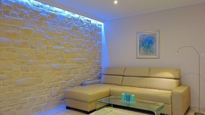 A room with a stone wall, a beige sofa, a glass coffee table, and a floor lamp. - Big Blue Apartments - Superior One Bedroom Apartment with Terrace and Sea View (Superior 4) (Dubrovnik)