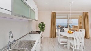 A modern kitchen with a sink, stove, and dining area with white chairs and a table. - Big Blue Apartments - Superior One Bedroom Apartment with Terrace and Sea View (Superior 4) (Dubrovnik)