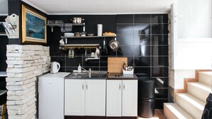 Une cuisine de taille réduite avec des meubles blancs, un dosseret de carrelage noir et un petit réfrigérateur.