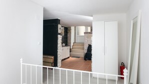 Une pièce avec un lit blanc, une balustrade blanche, une cuisine avec des placards blancs et un extincteur rouge.