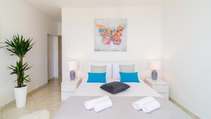 Een hotelkamer met een bed, twee nachtkastjes, een potplant en kleurrijke vlinderkunst aan de muur.