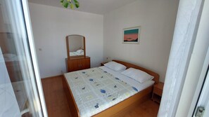 Een slaapkamer met een bed, een houten kledingkast, een nachtkastje, een spiegel en een ingelijste foto aan de muur.