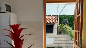 A kitchen with a microwave, a potted plant, and a view of a garden through an open door. - Apartments Matea - Two-Bedroom Apartment with Sea View and Balcony (Stikovica)