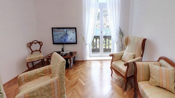 A living room with a wooden floor, two armchairs, a sofa, a television, and a window with curtains.