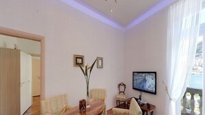 A living room with a wooden dining table, striped armchairs, a TV mounted on the wall, and a balcony with a view.
