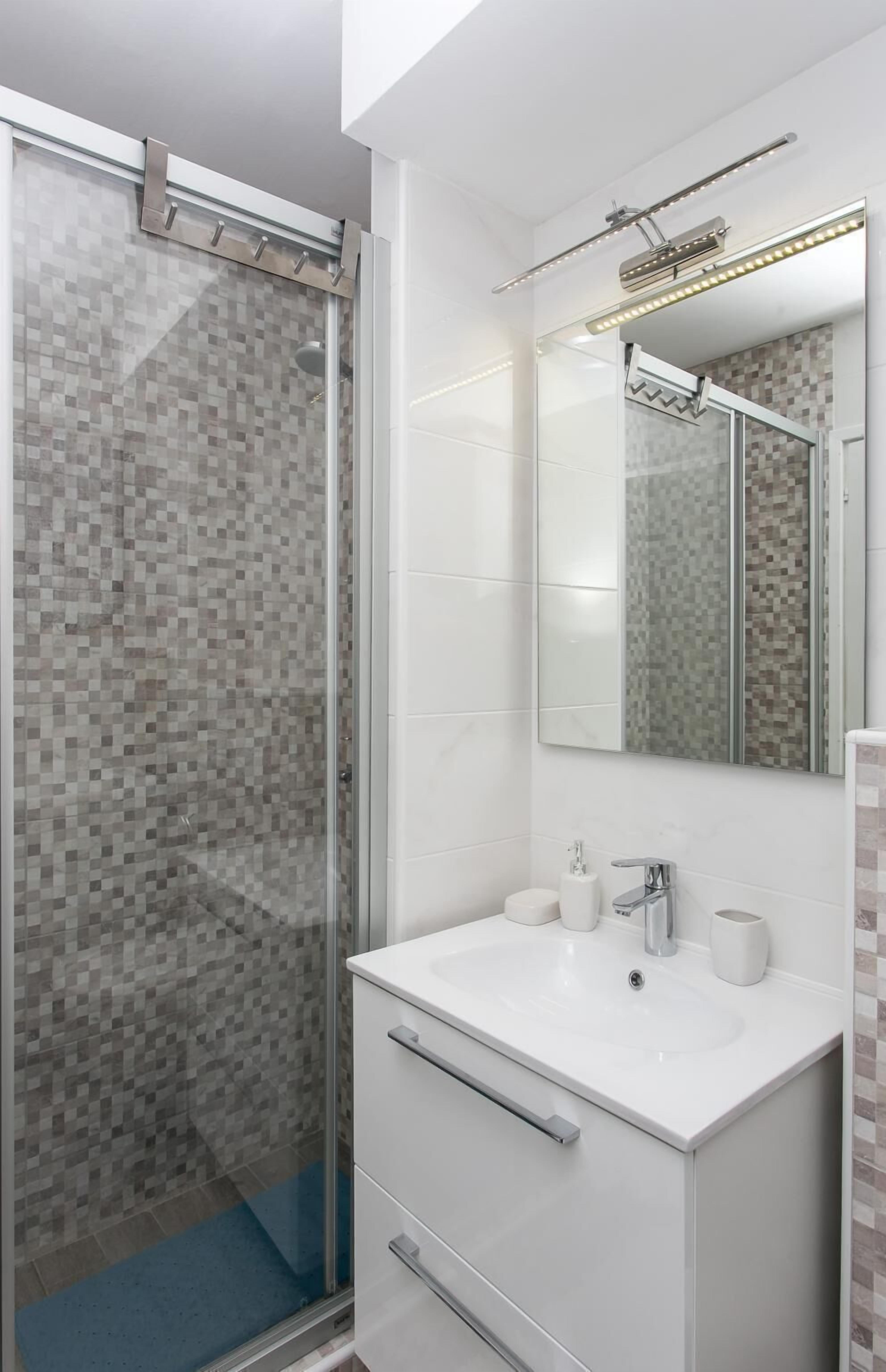 A modern bathroom with a glass shower enclosure, a white vanity with a mirror, and a tiled backsplash.