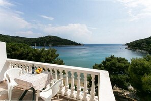 A balcony with a table set for two, overlooking a coastal bay with boats and greenery.