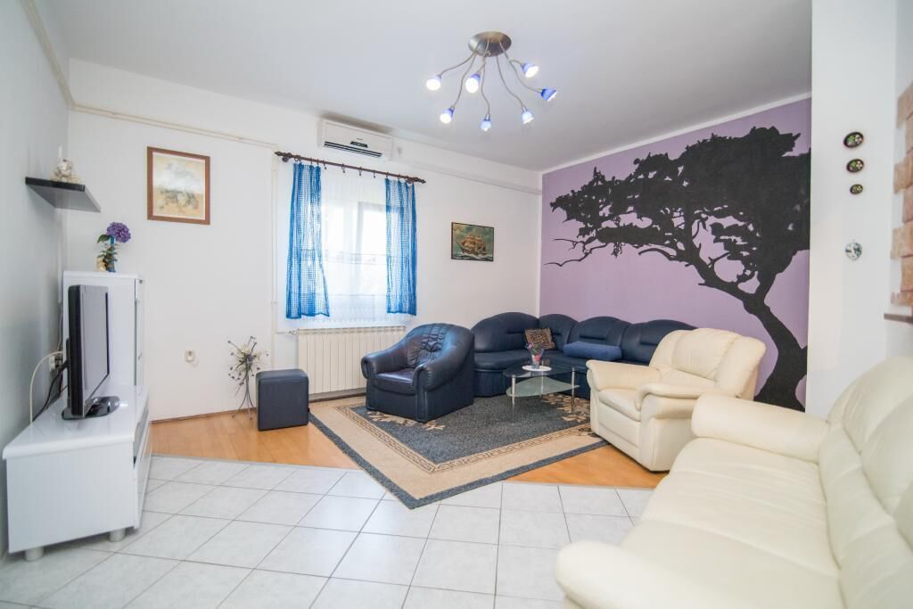 A living room with a TV, two sofas, a coffee table, and a decorative tree mural.