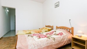 Un dormitorio con dos camas individuales, una mesita de noche con lámpara y una puerta que da a otra habitación.