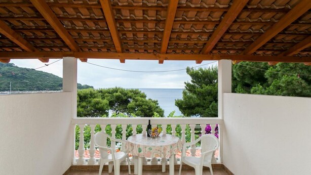 Un espacio de estar techado al aire libre con mesa y sillas, con vistas a un paisaje marino y de vegetación.