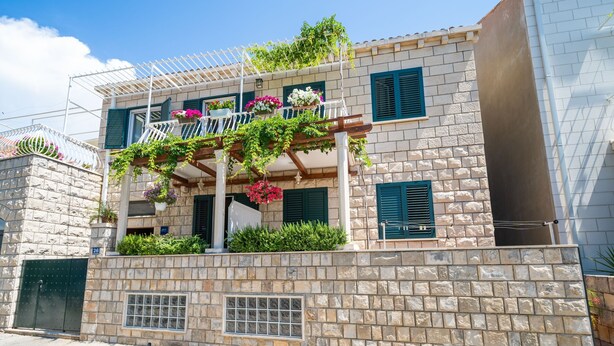 A two-story building with a stone facade, green shutters, and a balcony with hanging plants. - Apartments Villa Ivka - Studio Apartment (Dubrovnik)