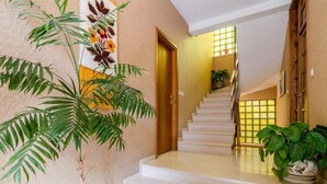 A staircase with white steps leading to a landing, surrounded by walls with a textured finish and a large potted plant on the right. - Apartments Villa Ivka - Studio Apartment (Dubrovnik)