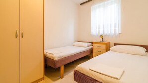 A bedroom with two single beds, a wardrobe, a bedside table with a lamp, and a window with sheer curtains. - Apartments Villa Ivka - Studio Apartment (Dubrovnik)