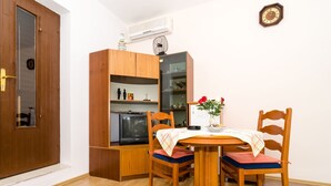 A compact living space with a wooden dining table, two chairs, a small cabinet, and a television. - Apartment Berk - One-Bedroom Apartment with Terrace (Dubrovnik)