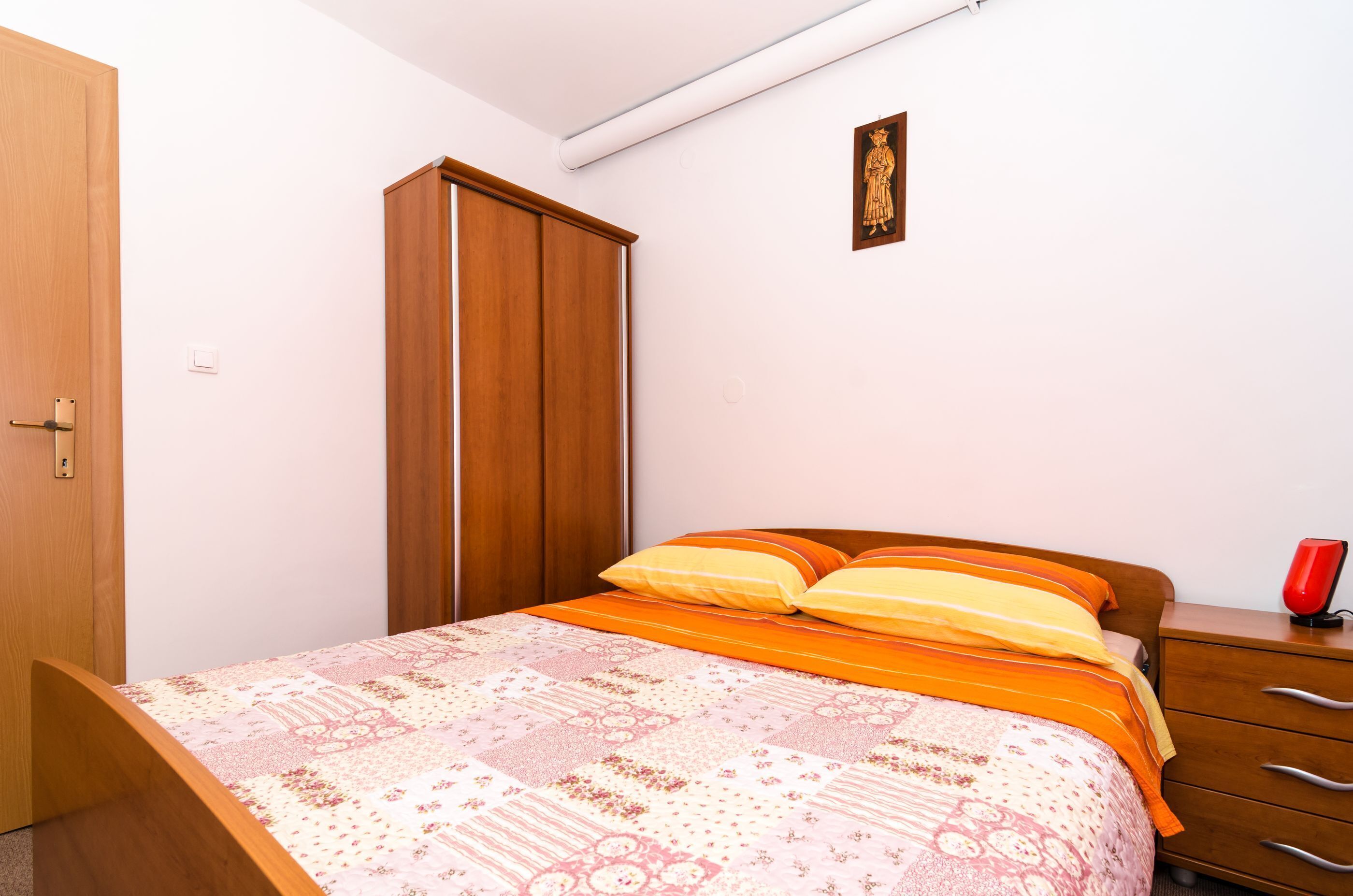 A bedroom with a bed, wooden wardrobe, and a nightstand.