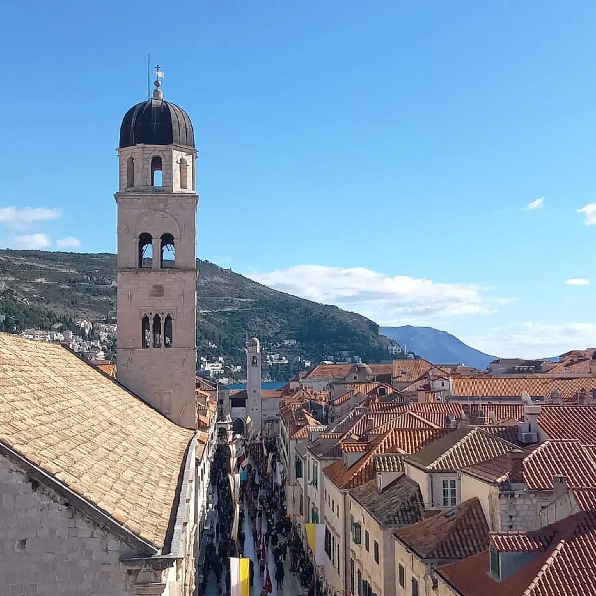 A historic tower with a dome and bell, surrounded by traditional buildings with red-tiled roofs.