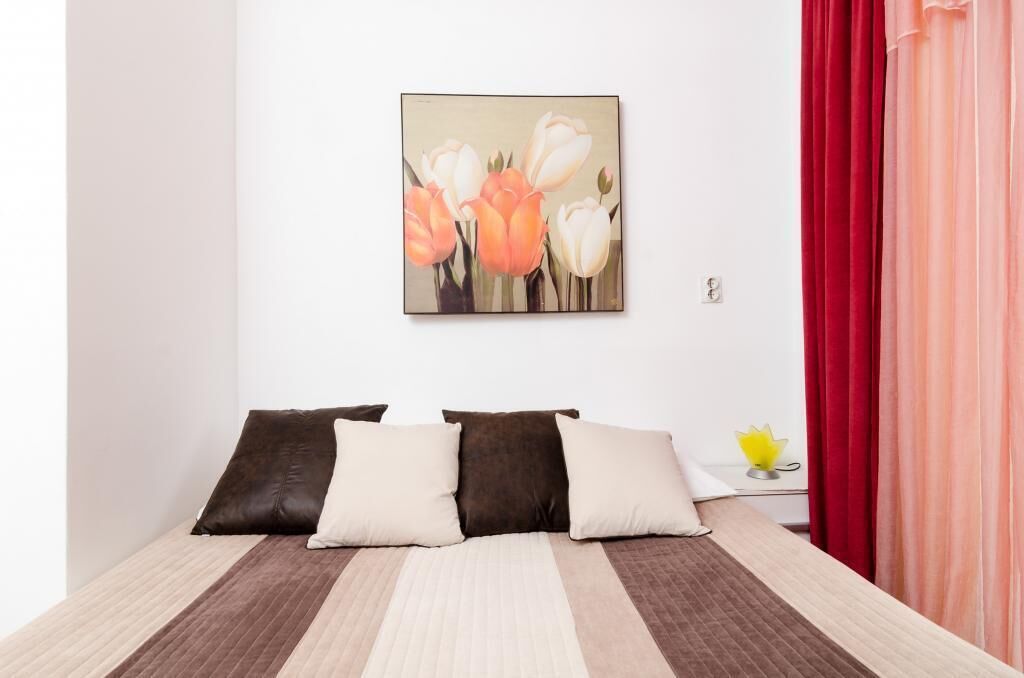 A bedroom with a bed, pillows, a wall-mounted painting, and a nightstand with a lamp.
