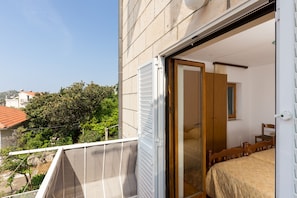 A balcony with a white mesh screen, a wooden bed with a beige bedspread, and a wooden chair. - Apartments Kisic-Three Bedroom Apartment with Sea View (Mlini)