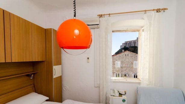 A bedroom with a bed, wooden wardrobe, and a window with a view of a stone building. - Rooms Pile - Double Room with Patio (Dubrovnik)