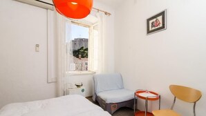 A hotel room with a bed, a chair, a small table, and a window with a view of buildings. - Rooms Pile - Double Room with Patio (Dubrovnik)
