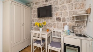 A compact kitchen with a stone wall, a flat-screen TV, a sink, and a small dining area with two chairs and a table. - Guest House Lumin - Double Room with City View (First Floor) - (BR1) (Dubrovnik)