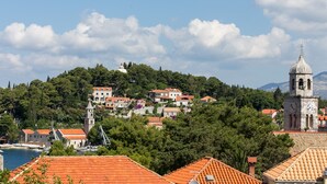 A coastal town with terracotta-roofed buildings, a prominent clock tower, and a church on a hill.
