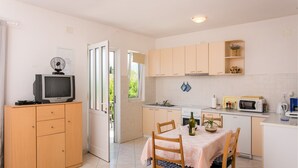 A compact kitchen with a dining area, a television on a cabinet, and a window providing natural light.