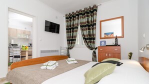 A hotel room with a bed, a TV, a desk with a chair, a microwave, and a window with curtains. - Apartments Kapelica - Studio apartment (Dubrovnik)