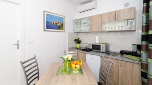 A compact kitchen with a dining table, chairs, a microwave, and a small refrigerator. - Apartments Kapelica - Studio apartment (Dubrovnik)