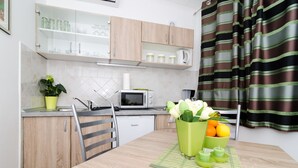 A modern kitchen with wooden cabinets, a microwave, and a dining area with a table set for two. - Apartments Kapelica - Studio apartment (Dubrovnik)