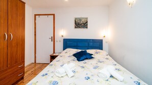 Een slaapkamer met een houten garderobe, een bed met een bloemenbedekking, twee wandlampen en een schilderij aan de muur.