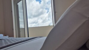 Una habitación de hotel con una cama, un ventanal y una puerta que da a un balcón exterior.