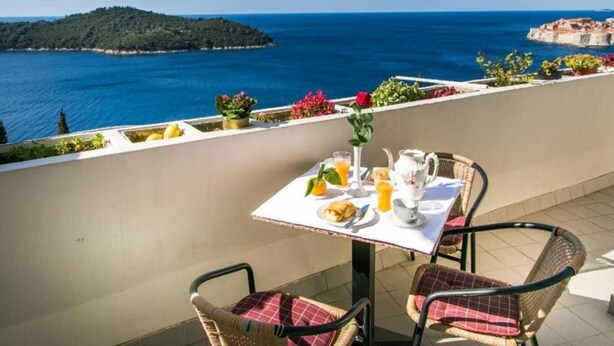 Una terraza con una mesa preparada para el desayuno, con vistas a la costa, una isla distante y el mar.
