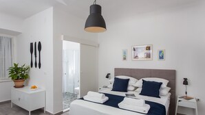 Quarto de hotel moderno com uma cama grande, uma mesa de cabeceira, um criado-mudo, uma planta em vaso e vista para o banheiro.