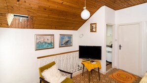 Un accogliente soggiorno con travi in legno a soffitto, una televisione a schermo piatto e un'area pranzo con tavolo giallo.