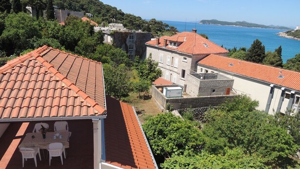 Un edificio residenziale con tetto in tegole rosse, un balcone con tavolo e sedie e vista sul mare.
