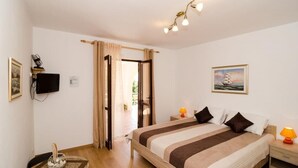Un dormitorio con cama, lámparas de noche, televisor, un cuadro y ventana con cortinas.