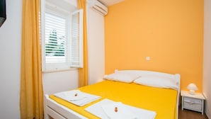 Une chambre à coucher avec une couvre-lit jaune, des oreillers blancs et une table de chevet blanche sur laquelle se trouve une lampe.