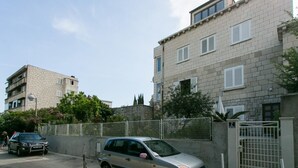 Un immeuble d’habitation avec une entrée sécurisée par un portail, une voiture garée et un ciel dégagé.