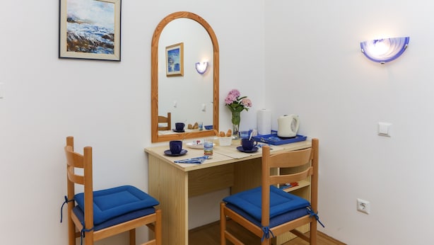 A small, tidy room with a wooden desk, two chairs, a mirror, a framed painting, a vase with flowers, and a wall-mounted light fixture. - K-Apartments - Double or Twin Room with Garden View - A3 (Dubrovnik)