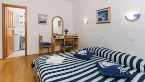 A bedroom with a bed, a desk, a chair, a mirror, and a door leading to a bathroom. - K-Apartments - Double or Twin Room with Garden View - A3 (Dubrovnik)