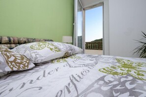A bedroom with a bed, pillows, a nightstand, a lamp, and a view of a balcony.