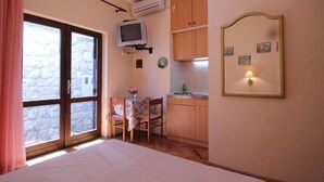 A bedroom with a large bed, a small table with a chair, a kitchenette, and a sliding glass door leading to a balcony. - Apartments Magda- Standard Backside Studio Apartment (Cavtat)