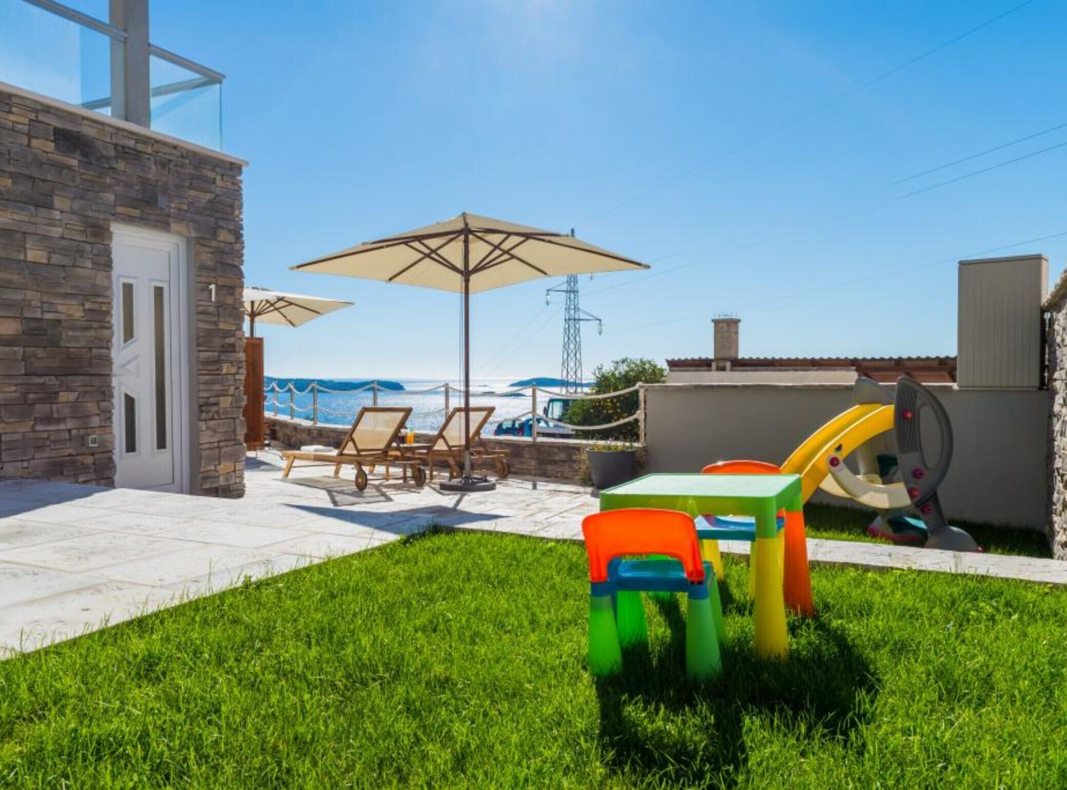 Een terras met tuinmeubilair, een speelruimte en uitzicht op zee.