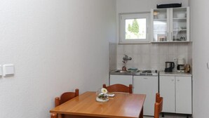 Ett kompakt kök med ett matbord och stolar, ett fönster ovanför diskhon och ett litet skåp med porslin.