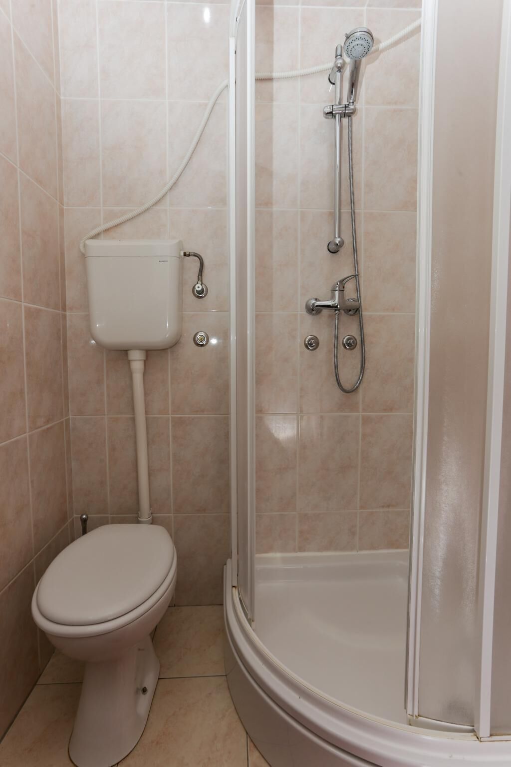 A bathroom with a toilet, a shower enclosure, and a wall-mounted toilet tank.